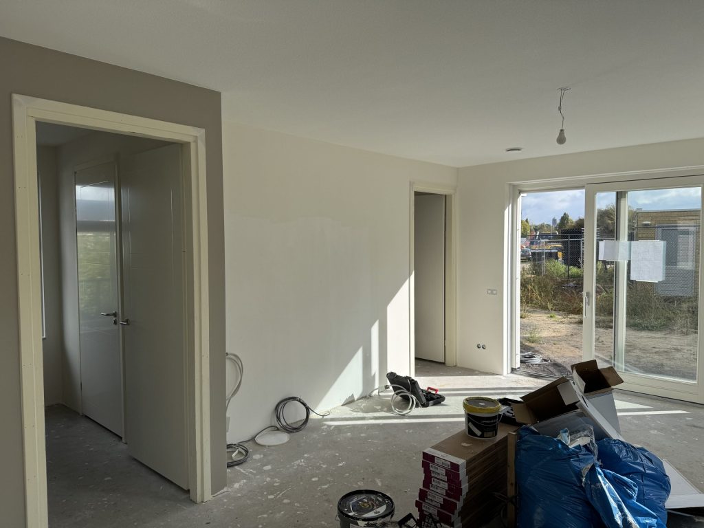 Woonkamer in een nieuwbouwwoning tijdens de afwerking, met verfemmers en schuifpui naar de tuin
