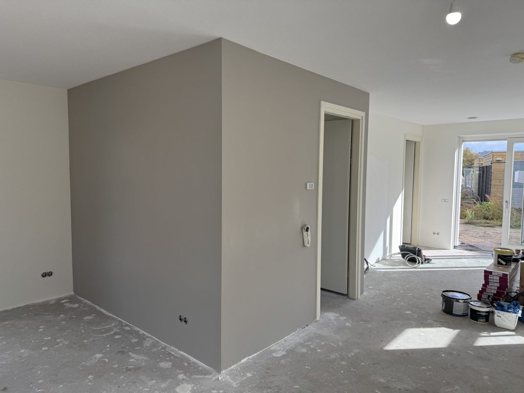 Afgewerkte wand in warm grijs naast witte muren in een nieuwbouwwoning met open schuifpui