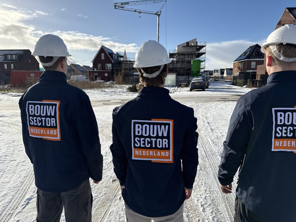 Drie vakmensen van Bouwsector Nederland met witte helmen op een besneeuwde nieuwbouwlocatie met een bouwkraan